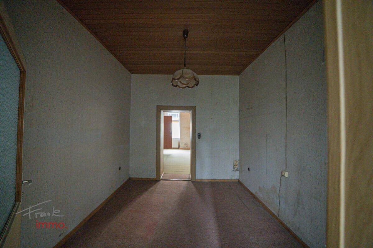 Langer Raum mit Teppichboden und Holzpaneeldecke, der auf eine Renovierung wartet.
