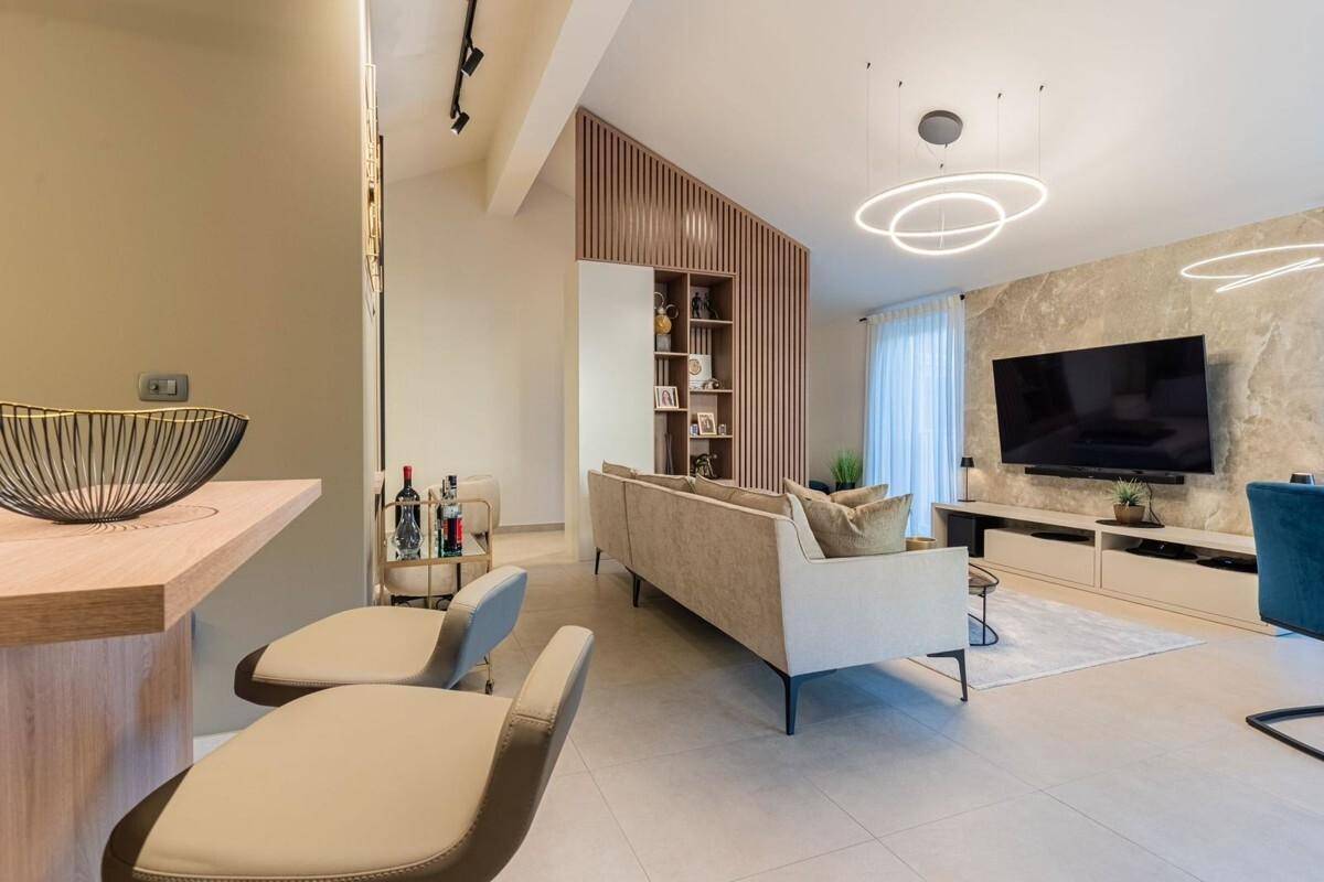 Geräumiger Wohnbereich mit beigem Sofa, Essbereich und einer kleinen Bar, durch Holzelemente abgetrennt.