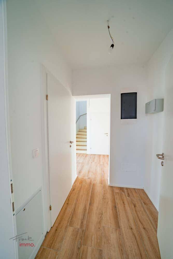 Heller Flur mit Holzoptikboden und Zugang zu weiteren Räumen sowie einer Treppe.