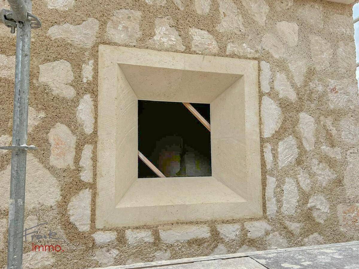 Detailansicht einer Natursteinmauer mit einem quadratischen Fensterrahmen.