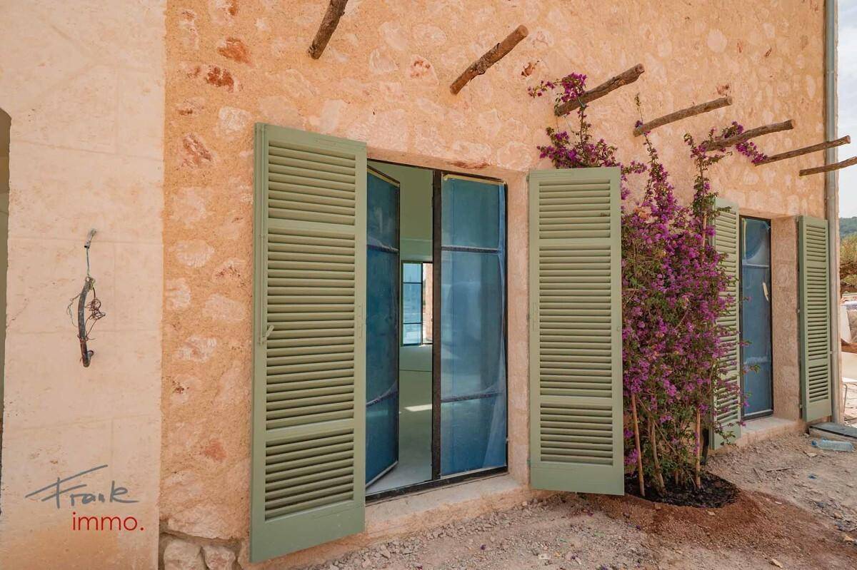 Detailansicht der rustikalen Steinfassade mit geöffneten grünen Fensterläden und blühender Kletterpflanze.