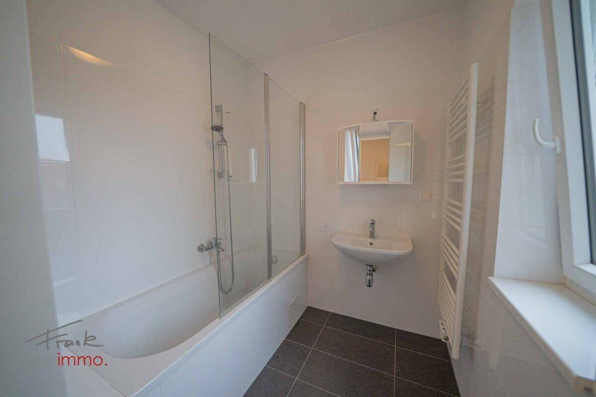 Modernes Badezimmer mit Badewanne, Duschwand, Waschbecken und beheiztem Handtuchhalter.