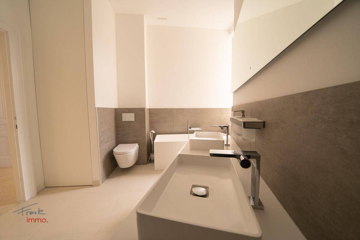 Modernes Badezimmer mit Doppelwaschbecken, Wand-WC und eleganten Fliesen in neutralen Farbtönen.