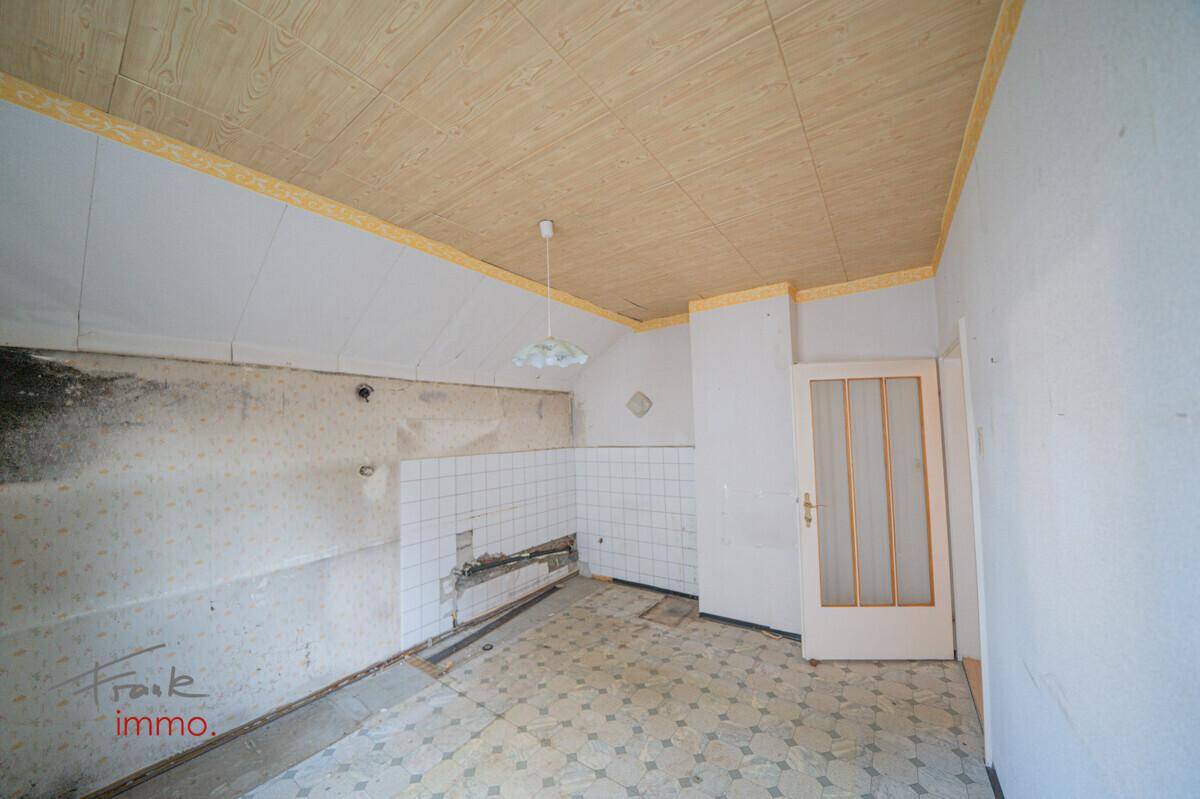 Renovierungsbedürftige Küche mit alten Fliesen, beschädigten Wänden und einer Holzdecke.