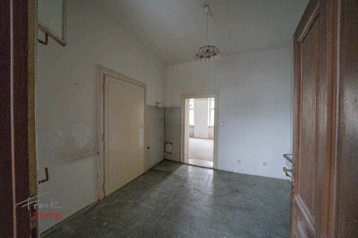 Einfacher Raum mit Waschbecken und einer Tür, die zu einem weiteren Zimmer führt.