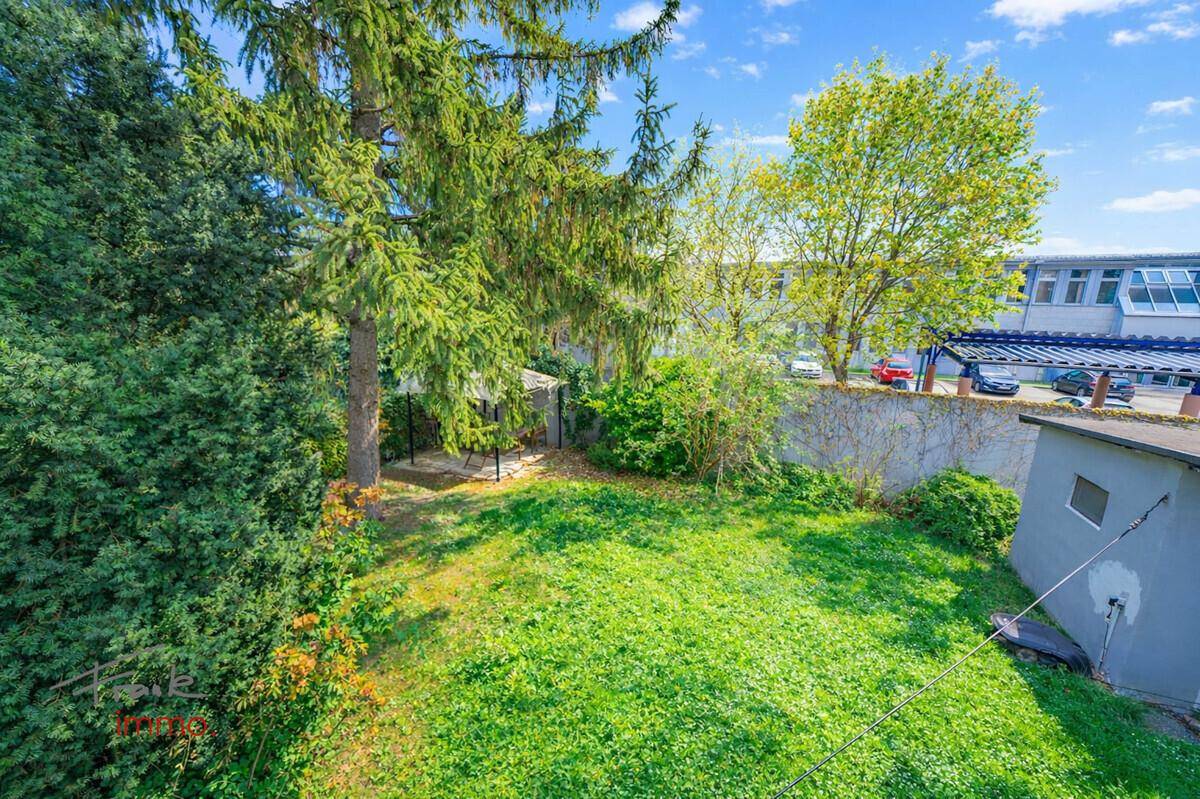 Weitläufiger Garten mit hohen Bäumen, Rasenfläche und einem kleinen Pavillon im hinteren Bereich.