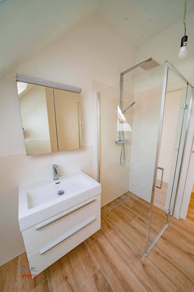 Modernes Badezimmer mit begehbarer Dusche, Waschbecken und Holzoptikfliesen unter Dachschräge.