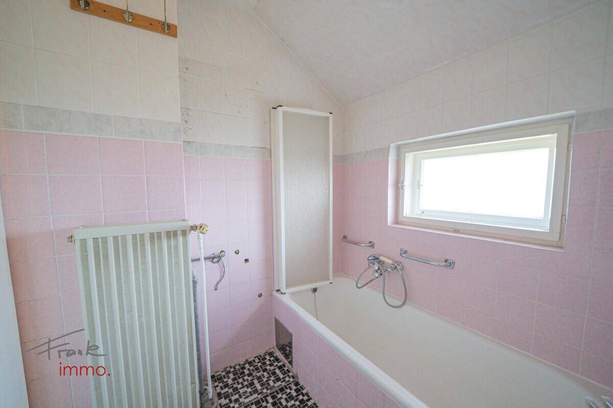 Badezimmer mit rosa Fliesen, Badewanne, Heizkörper und kleinem Fenster für natürliche Belüftung.