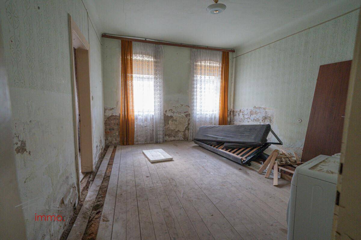 Renovierungsbedürftiger Raum mit abblätternder Tapete und alten Holzdielen.
