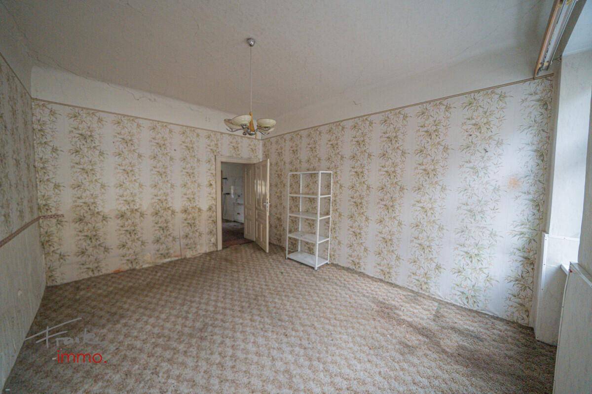 Zimmer mit gemusterten Tapeten, Teppichboden und einem einfachen Deckenlicht, renovierungsbedürftig.