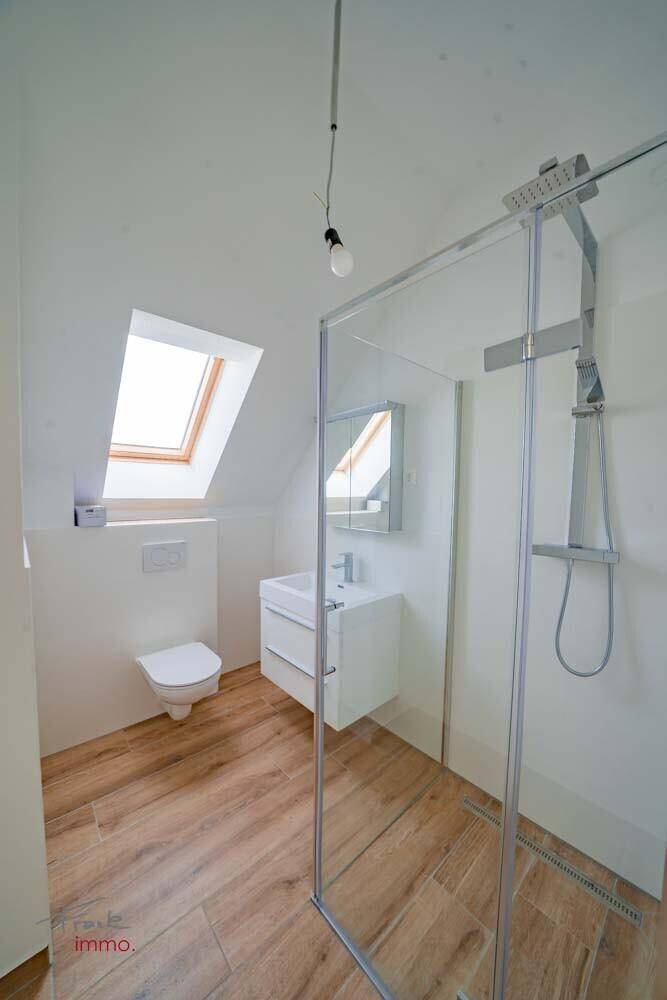 Modernes Badezimmer mit Dusche, Waschbecken, Toilette, Spiegelschrank und Dachfenster.