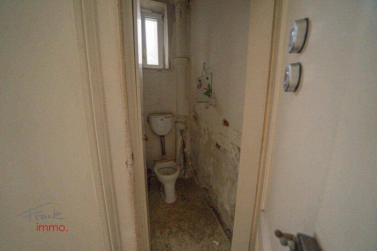 Kleines WC mit Toilette und Fenster, das auf eine Renovierung wartet.