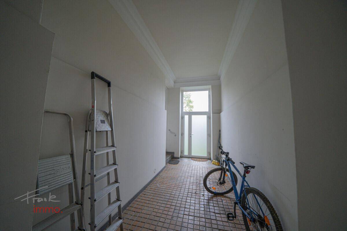 Heller Flur mit Fliesenboden, einer Leiter und einem Fahrrad, führt zu einer Glastür.