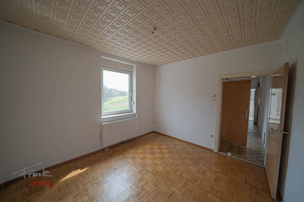 Geräumiges Zimmer mit Parkettboden, Fenster und Blick ins Grüne, bereit zur Einrichtung.