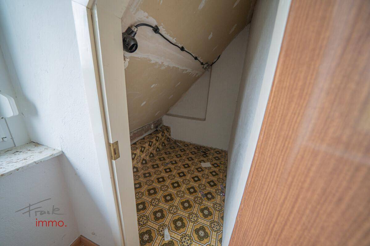 Kleiner Abstellraum unter der Dachschräge mit gemustertem Vinylboden und unfertigen Wänden.