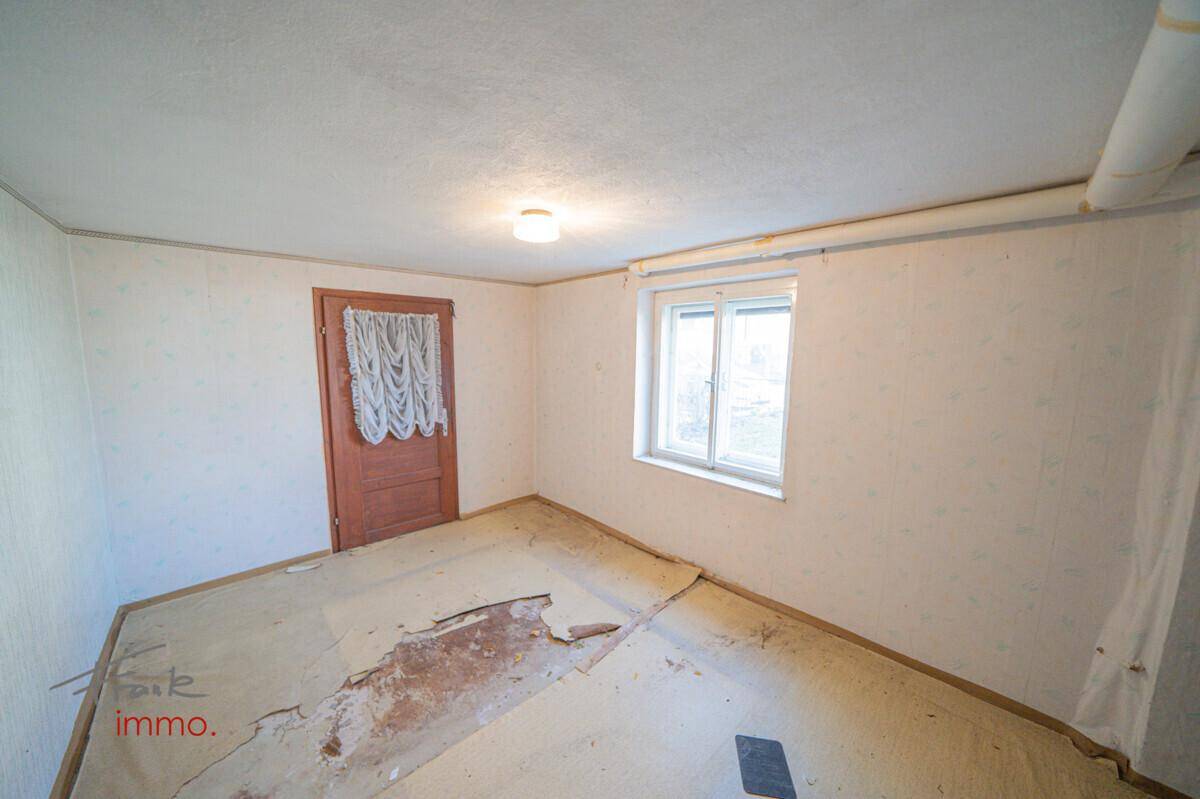 Helles Zimmer mit renovierungsbedürftigem Boden und Fenster, das viel Tageslicht hereinlässt.