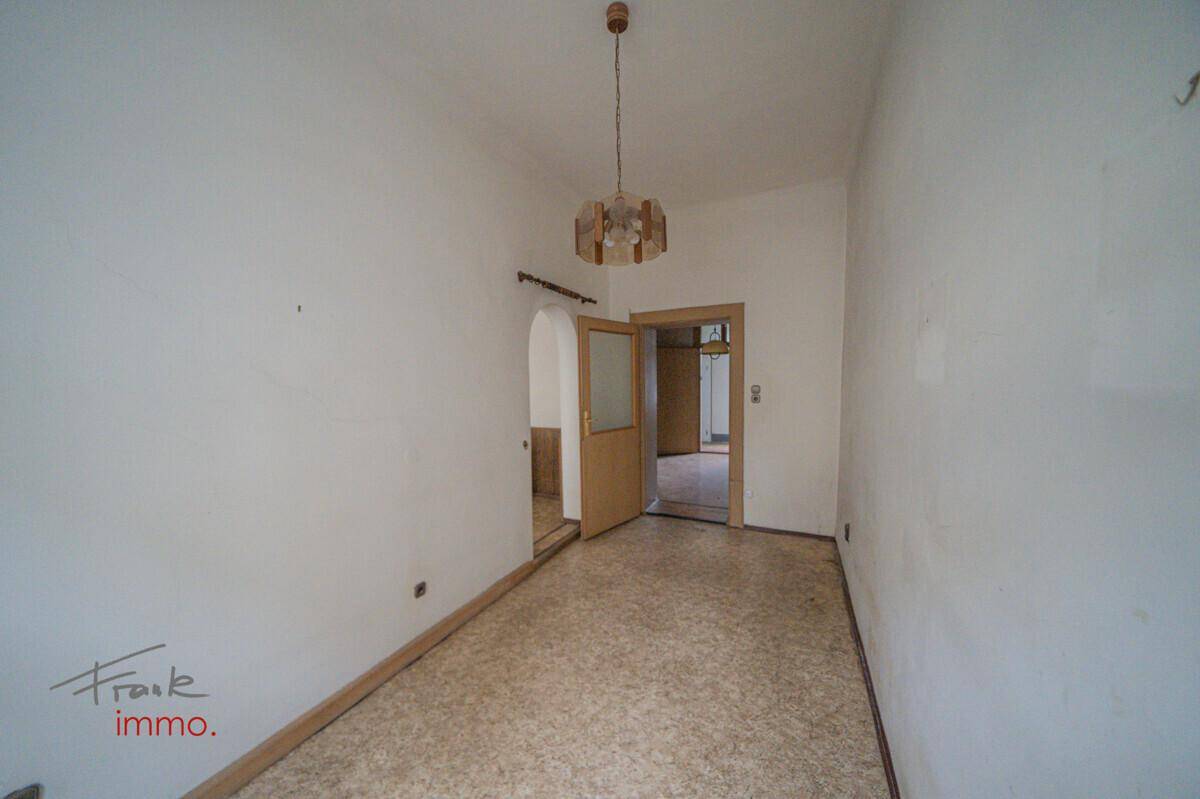 Schmaler Raum mit Linoleumboden und einer Tür mit Glaseinsatz, die zu einem weiteren Zimmer führt.