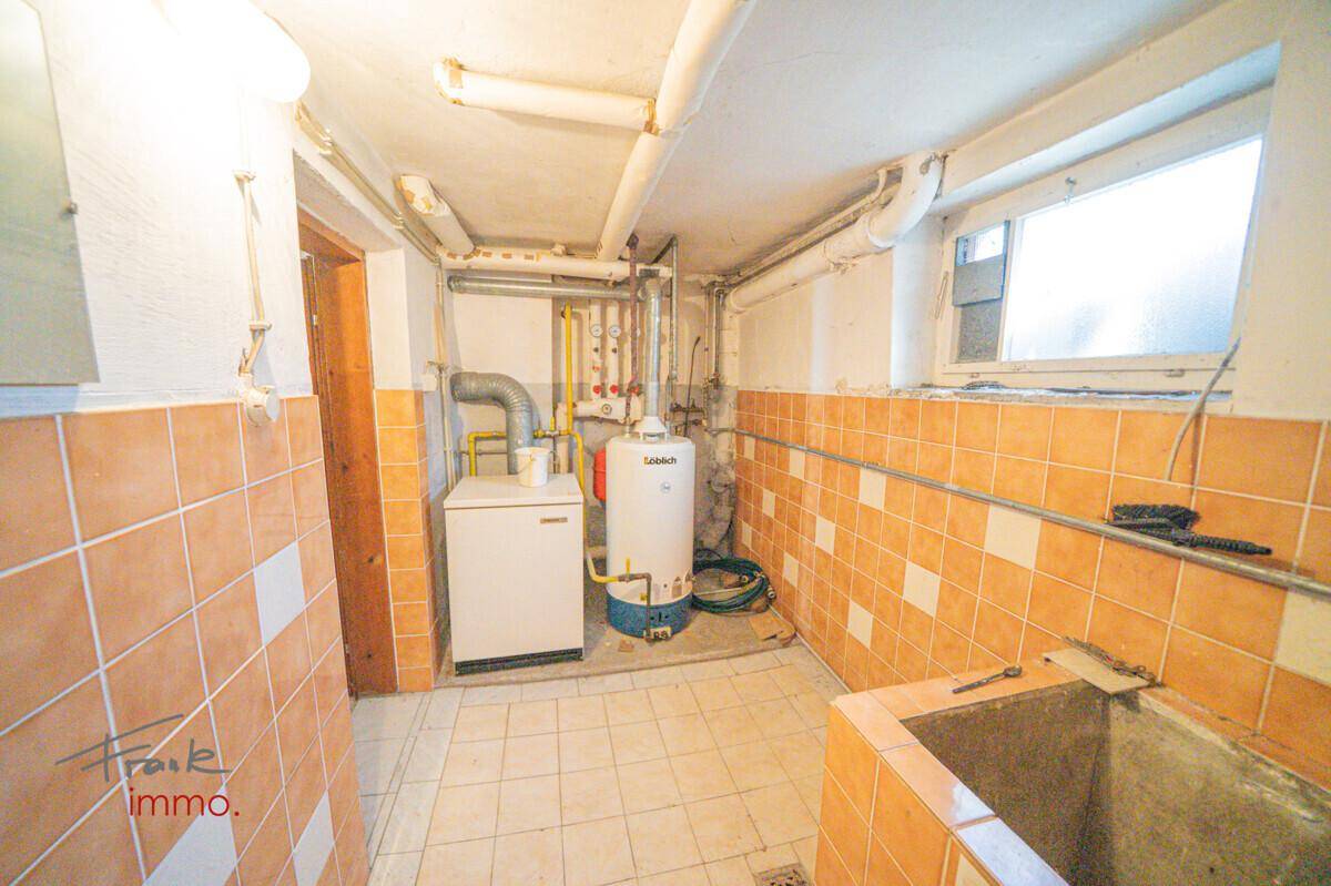 Hauswirtschaftsraum im Keller mit Heizkessel, Warmwasserspeicher und einem Waschbecken.