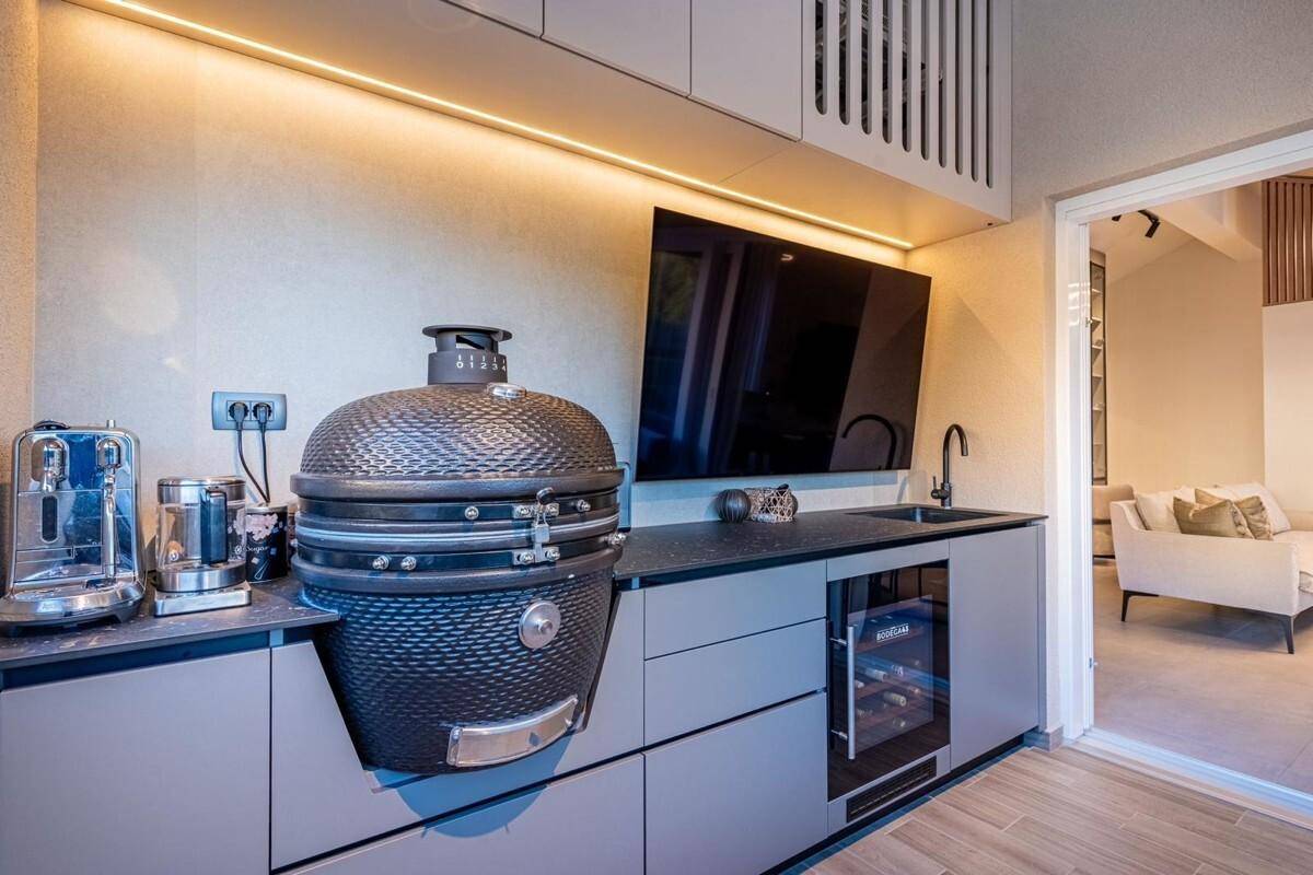 Moderne Außenküche mit Grill, Spüle und Weinkühler, angrenzend an den Wohnbereich.