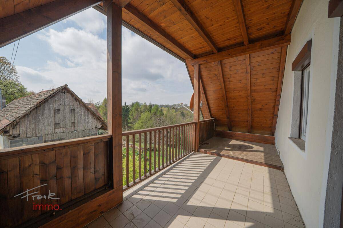 Geräumiger Holzbalkon mit weitem Blick über die grüne, hügelige Landschaft.