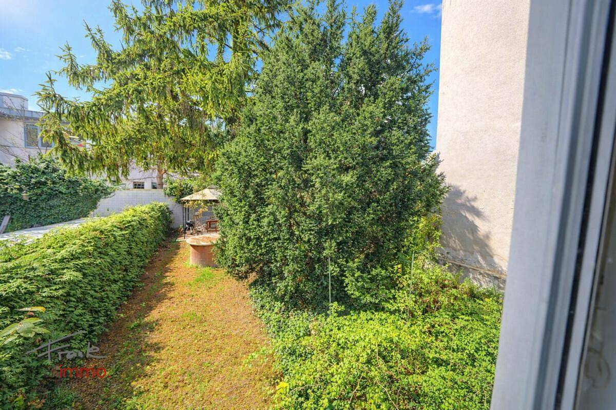 Blick aus dem Fenster auf einen grünen Garten mit hohen Hecken und einem kleinen Pavillon.