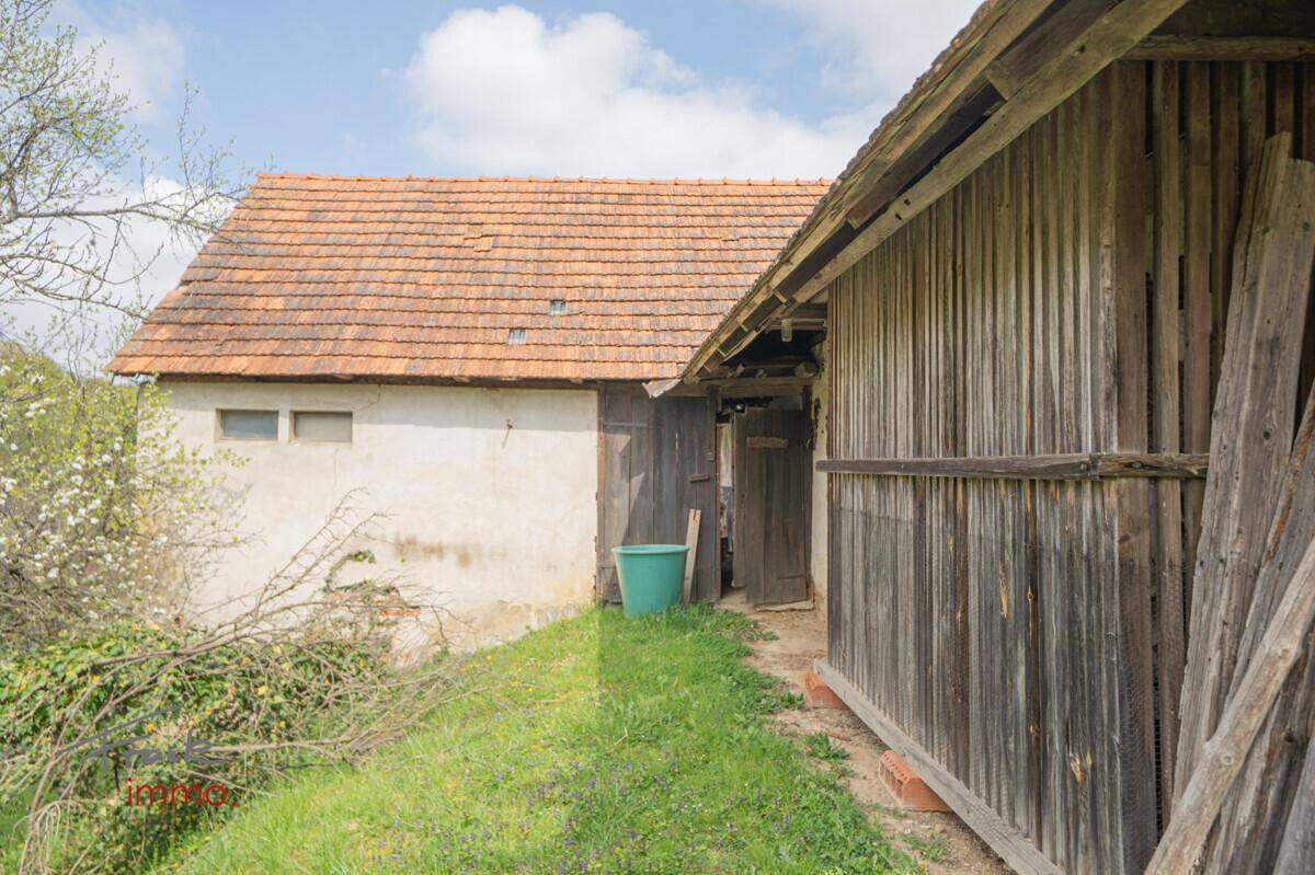 Seitenansicht eines alten Gebäudes mit Holzwänden und Ziegeldach, in ländlicher Umgebung.
