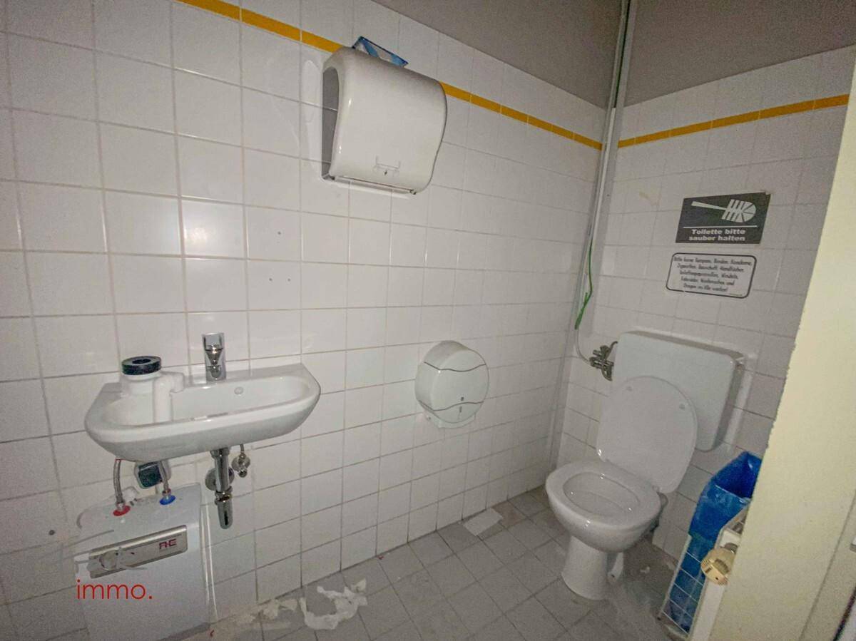 Einfache Toilette mit Waschbecken und weißen Fliesen an den Wänden, in gutem Zustand.