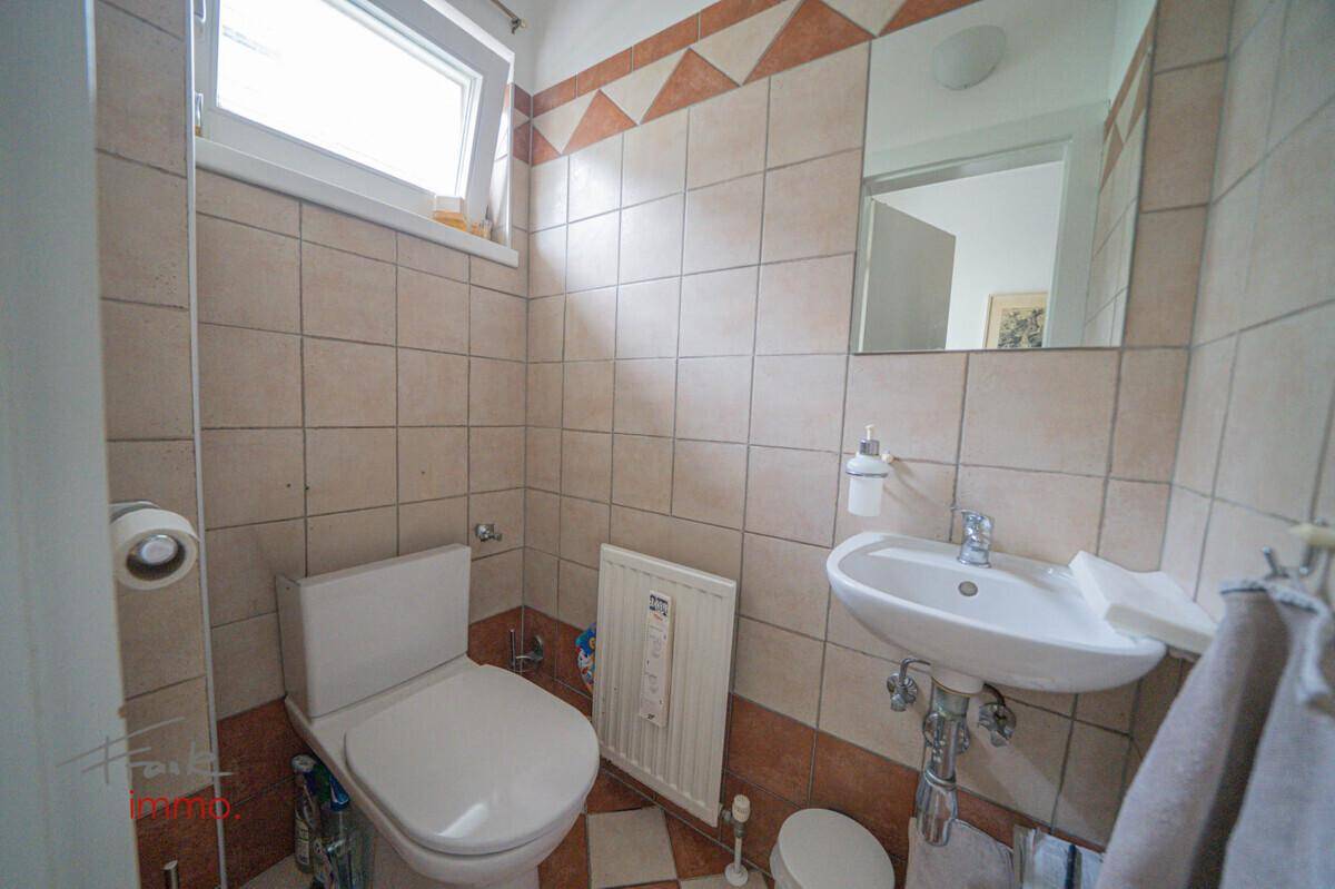 Kleines Gäste-WC mit beigefarbenen Fliesen, Fenster und einem einfachen Waschbecken.
