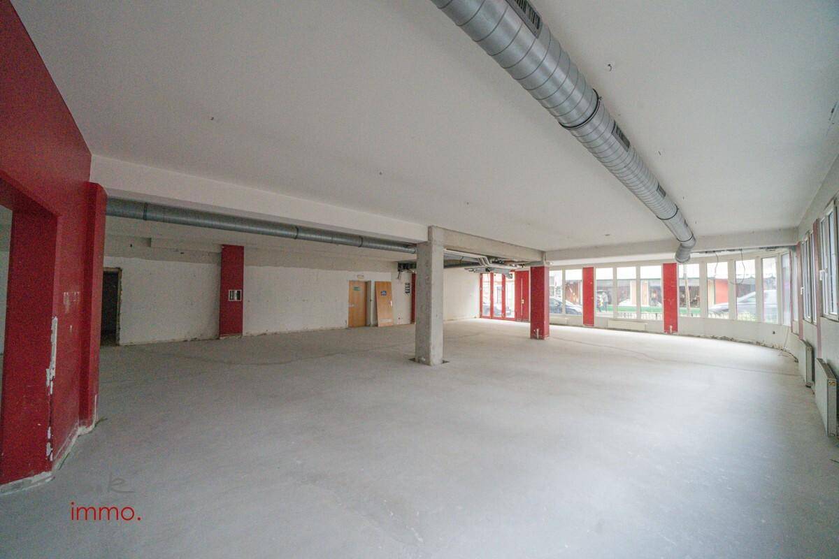 Großer, leerer Gewerberaum mit vielen Fenstern, roten Säulen und sichtbaren Deckeninstallationen.