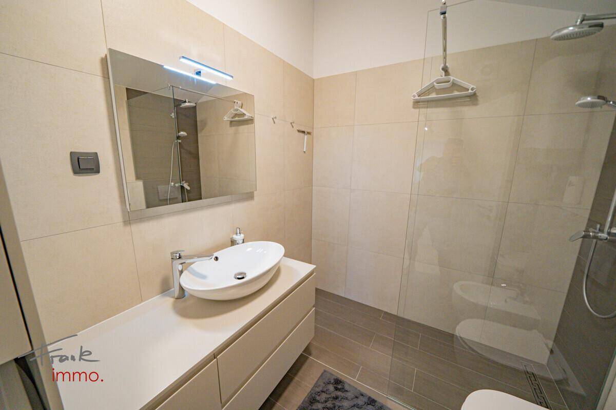 Modernes Badezimmer mit Aufsatzwaschbecken, begehbarer Dusche und großen Fliesen.