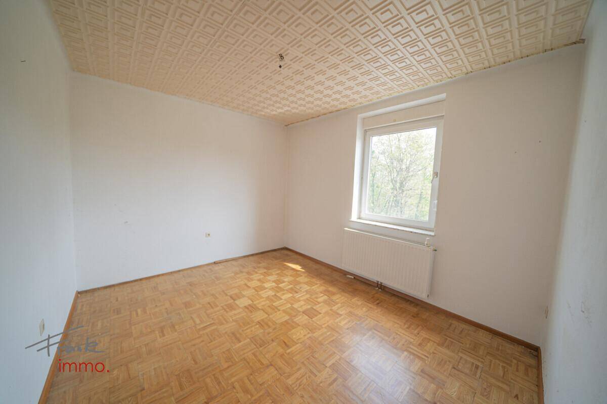 Helles, leeres Zimmer mit Parkettboden, Fenster und gemusterter Decke.