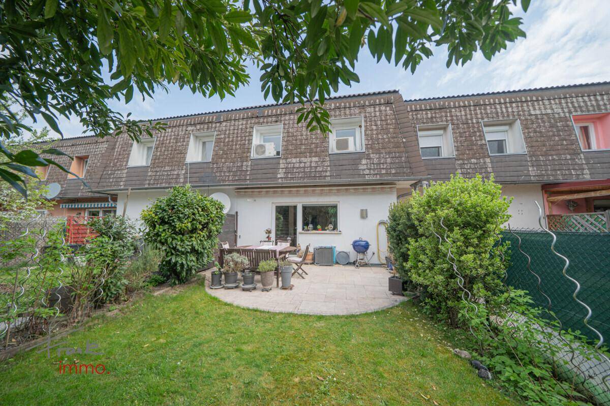 Rückansicht des Reihenhauses mit gepflegtem Garten und großer gepflasterter Terrasse.