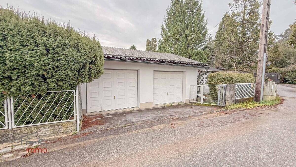Doppelgarage mit zwei weißen Toren und umgebender Hecke an einer Zufahrtsstraße.
