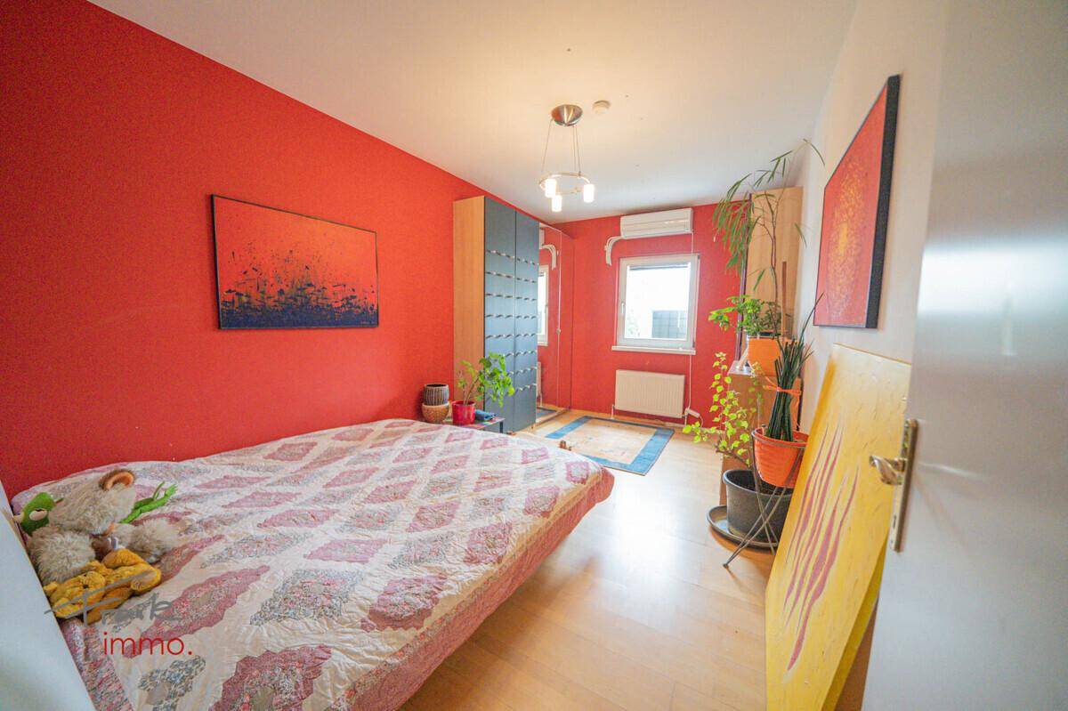 Farbiges Schlafzimmer mit Einzelbett, roter Akzentwand und Fenster für natürliches Licht.