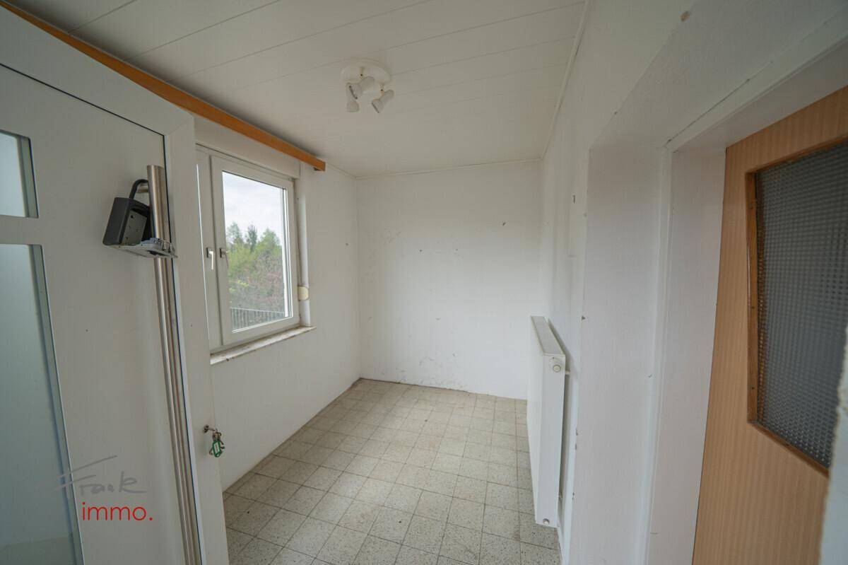 Kleiner, leerer Raum mit Fenster, Heizkörper und Fliesenboden, bereit zur Renovierung.