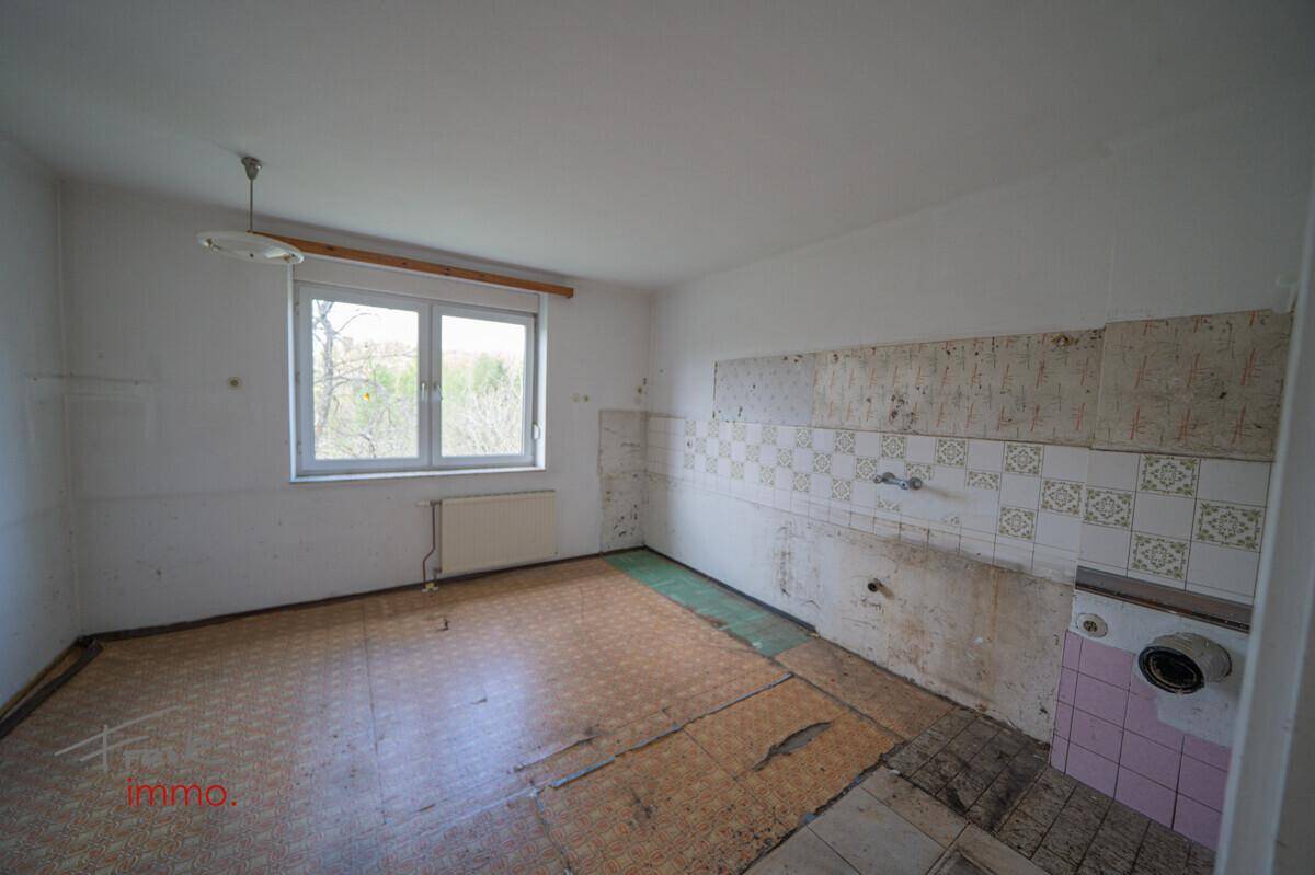 Leere Küche mit alten Wandfliesen, Fenster und Spuren einer ehemaligen Küchenzeile, renovierungsbedürftig.