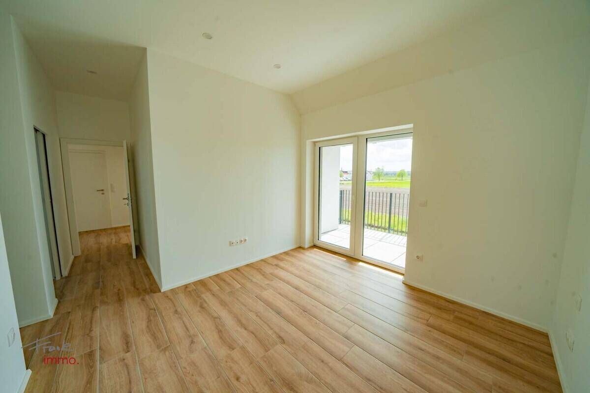 Geräumiges Zimmer mit Holzoptik-Fliesenboden und Zugang zu einem französischen Balkon.