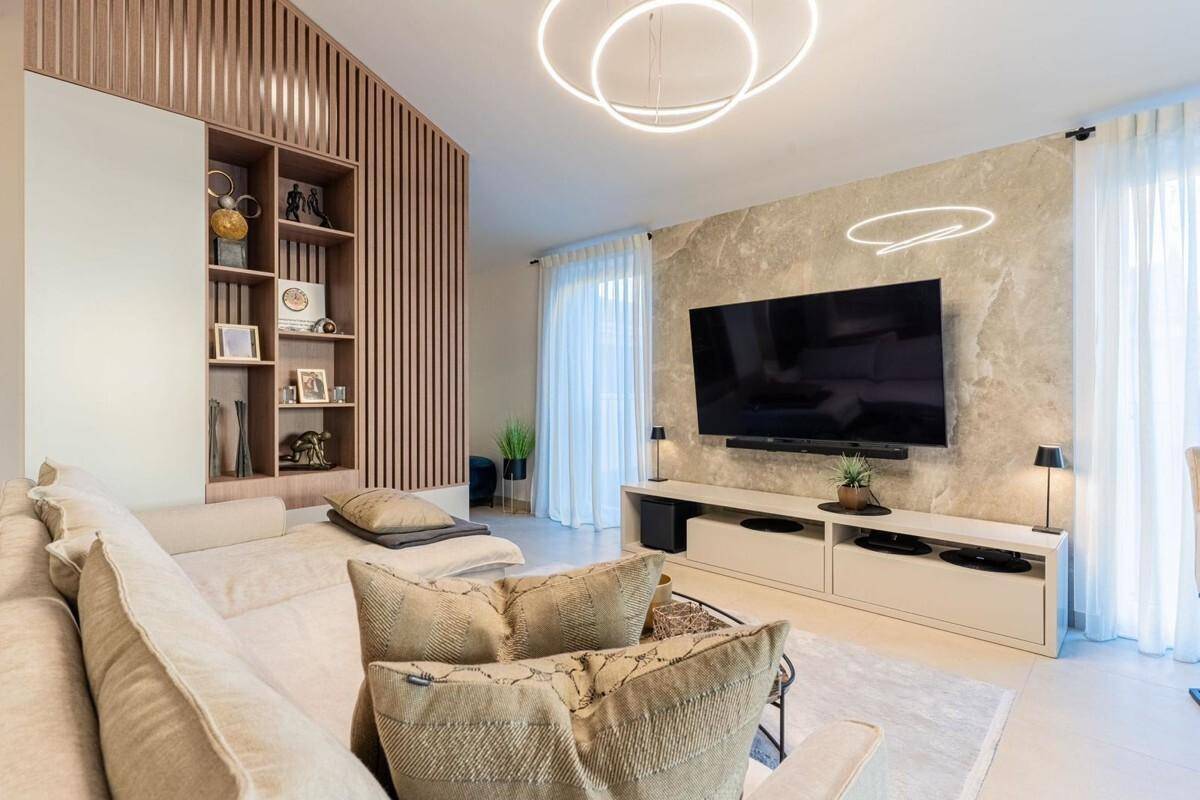 Modernes Wohnzimmer mit beigem Sofa, Holzwandverkleidung und großem Fernseher an einer Marmorwand.