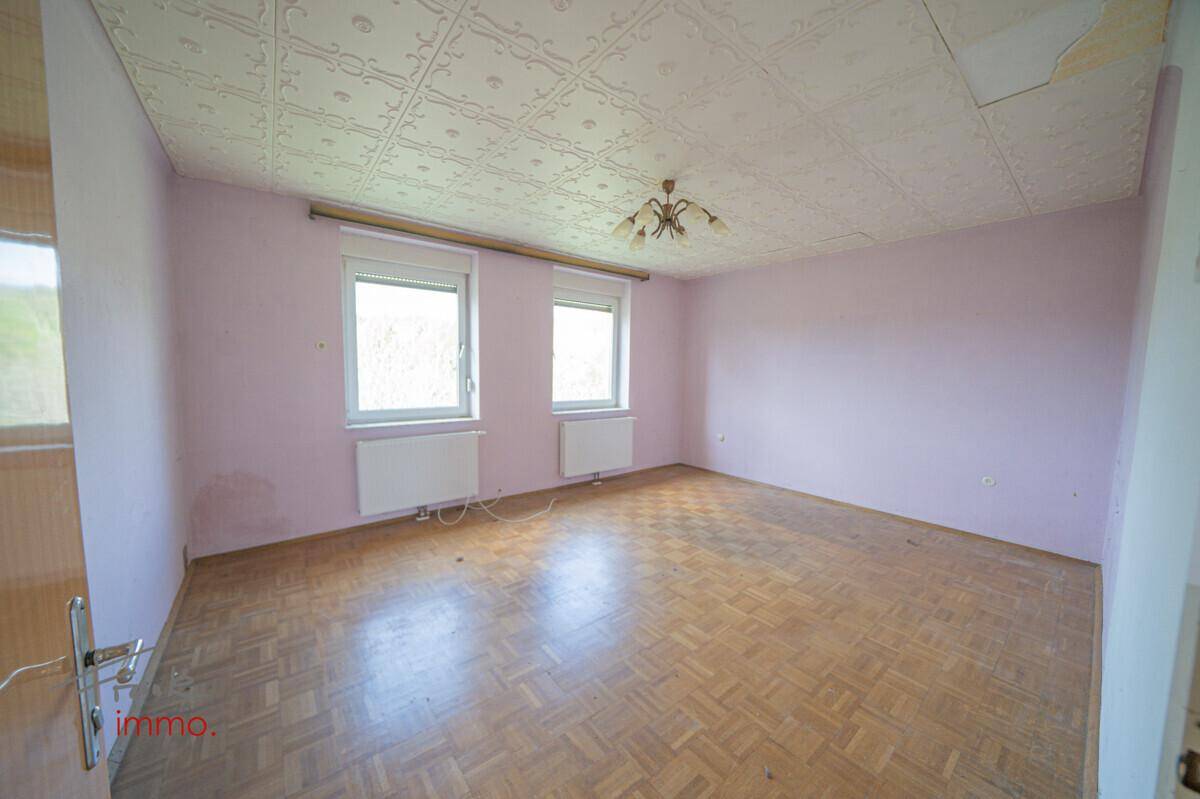 Helles Zimmer mit rosa Wänden, Parkettboden und zwei Fenstern, die viel Licht hereinlassen.