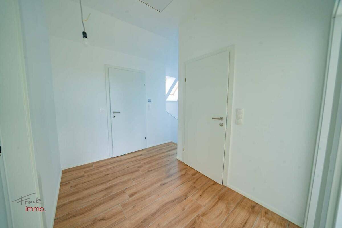 Obergeschoss-Flur mit Holzoptik-Fliesenboden und weißen Türen, der zu den Zimmern führt.