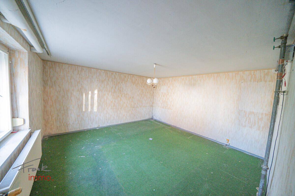 Geräumiges Zimmer mit grünem Teppichboden, Tapetenresten und einem Fenster, das Licht spendet.