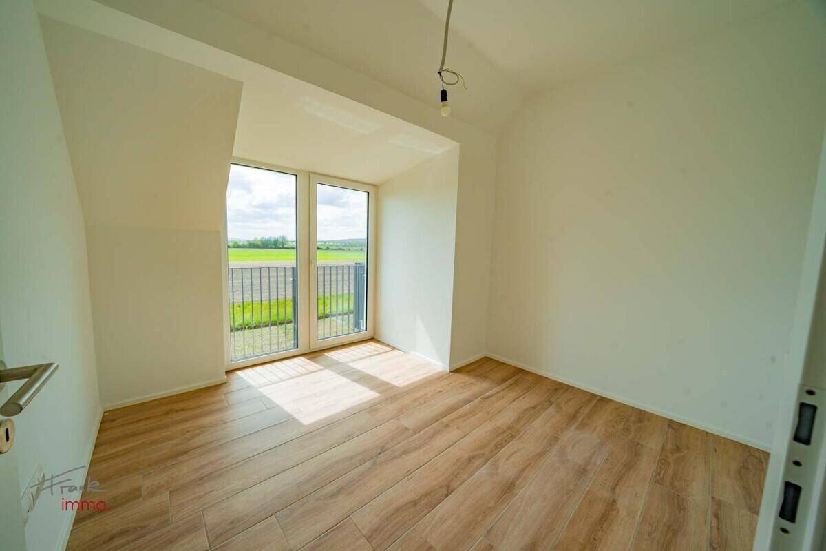 Helles Zimmer mit Holzoptik-Fliesenboden und Zugang zu einem französischen Balkon.