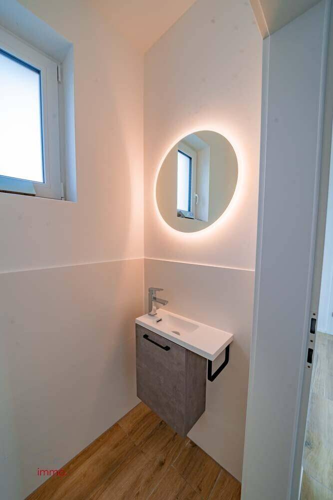 Modernes Gäste-WC mit wandhängendem Waschbecken, beleuchtetem Spiegel und Fenster.