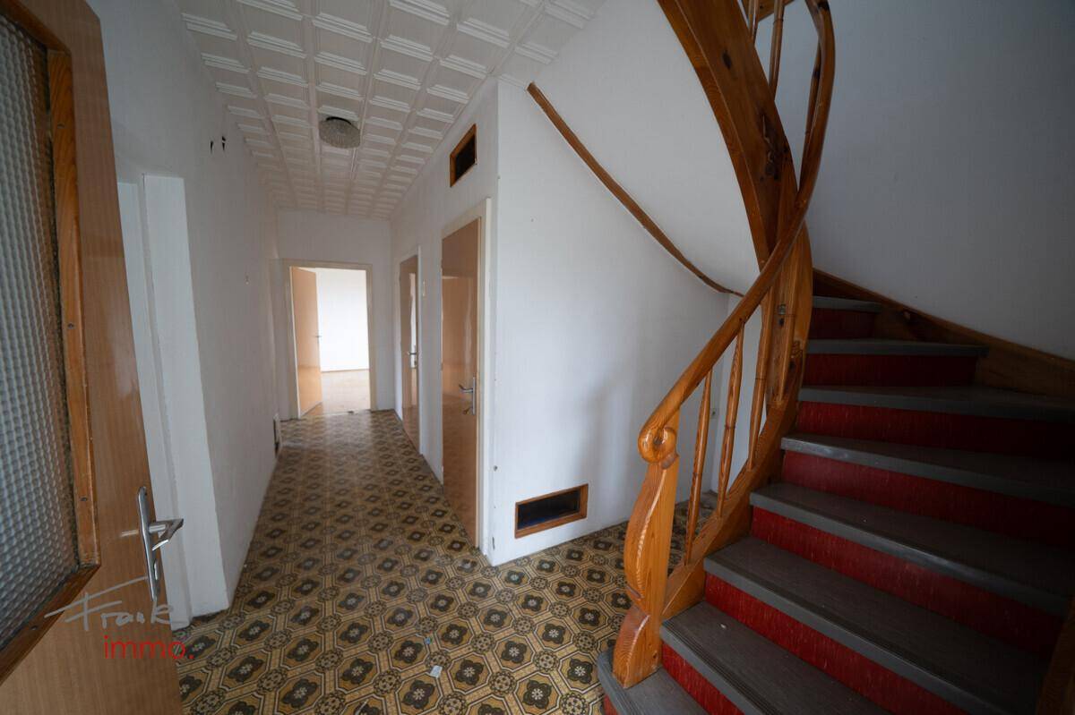 Flur mit gemustertem Fliesenboden und einer geschwungenen Holztreppe, die in die obere Etage führt.