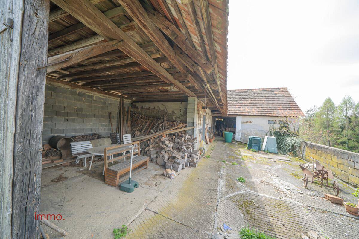 Überdachter Außenbereich mit Holzstapeln und Sitzgelegenheiten, ideal für Lagerung und Entspannung.