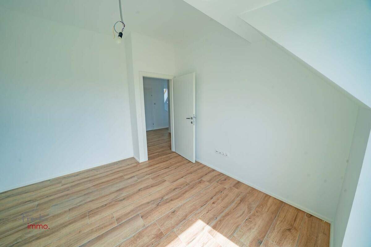 Geräumiges Zimmer mit Holzoptik-Fliesenboden und Blick ins Grüne durch die Fenster.