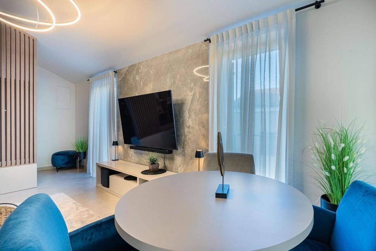 Moderner Essbereich mit rundem Tisch und blauen Stühlen, angrenzend an den hellen Wohnbereich.