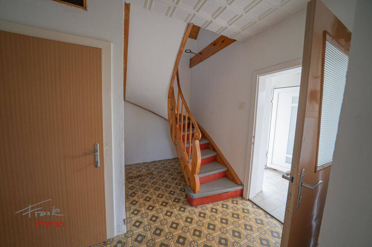 Flur mit Holztreppe und gemustertem Boden, der zu verschiedenen Räumen führt.