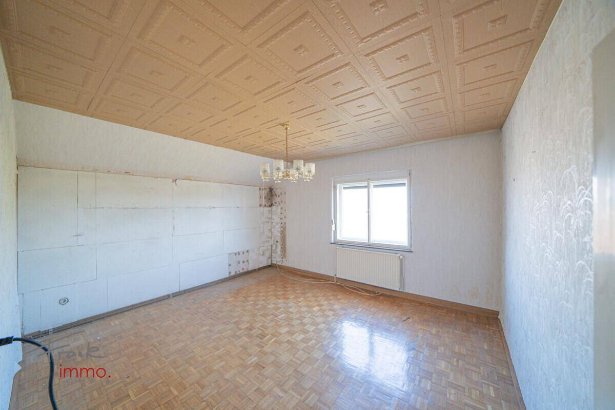 Heller Raum mit Parkettboden, Fenster und dekorativer Decke, ideal für ein gemütliches Wohnzimmer.
