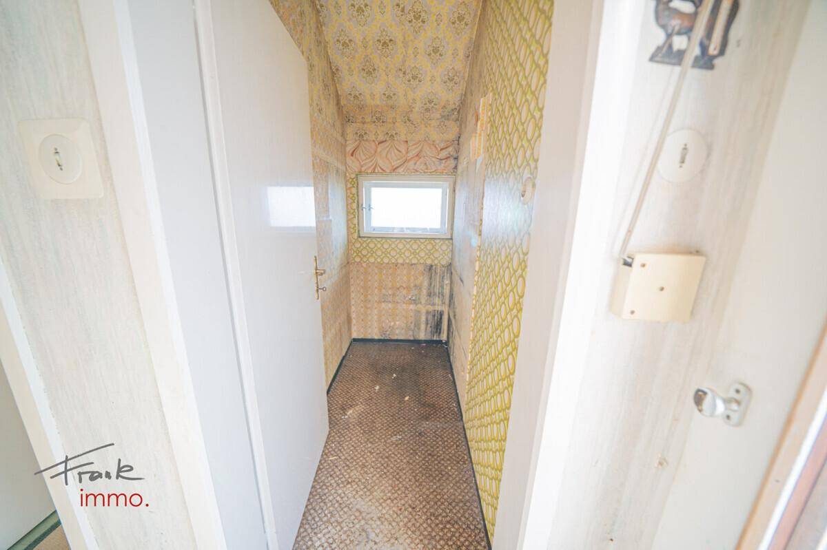 Renovierungsbedürftiges Gäste-WC mit gelber Tapete, Toilette und Fenster, bietet viel Gestaltungspotenzial.